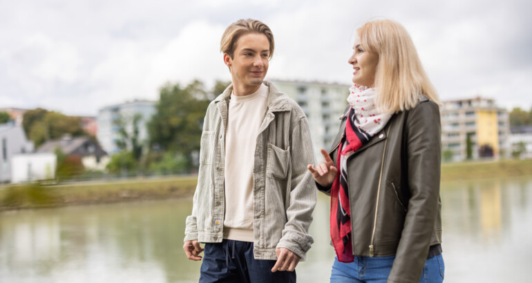Sozialpädagogin redet mit Jugendlichem, während die beiden am Flusssand gehen.