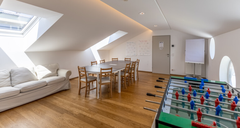 Innenansicht eines Zimmers der Wohngemeinschaft Tischfußballtisch, Couch und Esstisch.