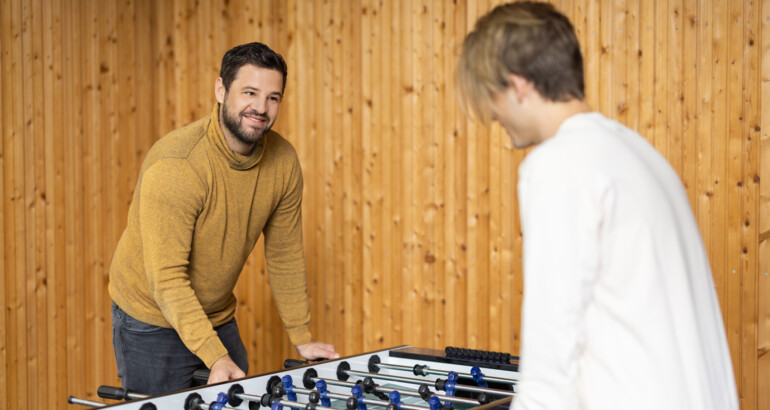 Sozialpädagoge spielt Tischfußball mit Jugendlichem. 