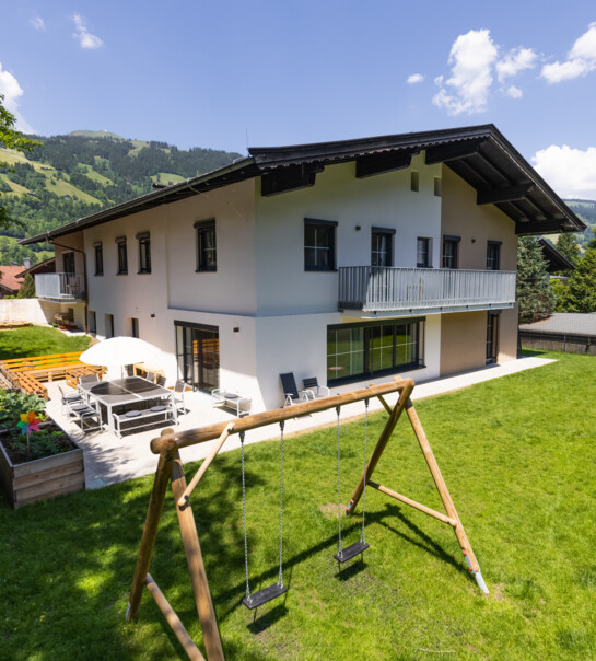 Außenansicht der Wohngemeinschaft mit Garten, Schaukel und Esstisch mit Schirm.