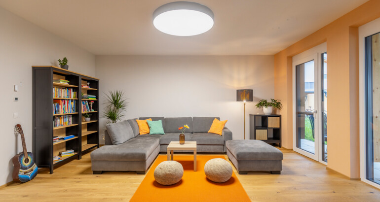 Innenansicht eines Schlafzimmers der Wohngemeinschaft mit Bett, Regalen und Schreibtisch. Fenster erlauben viel Licht in das Zimmer.